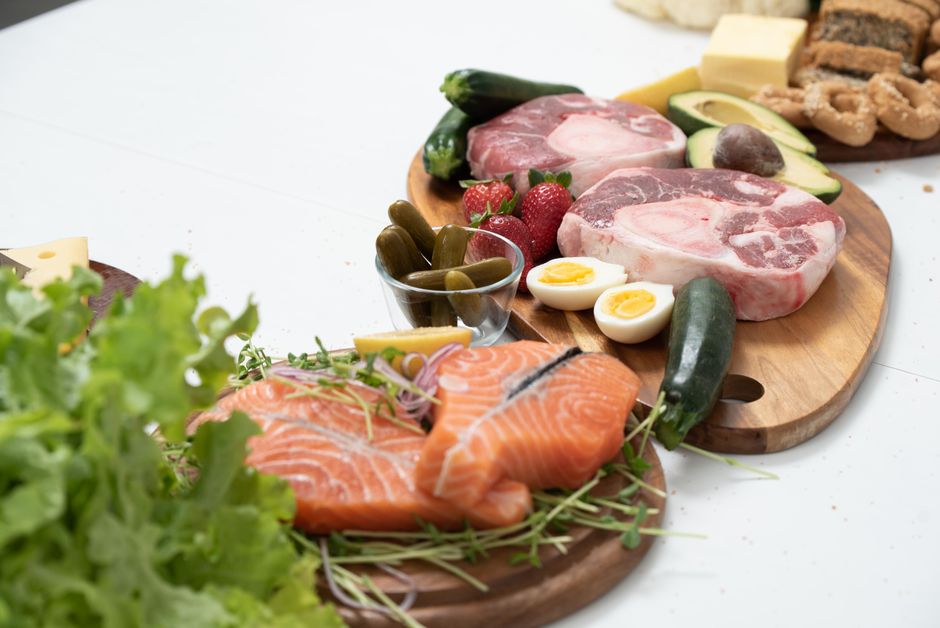 Färska ingredienser för ketogen kost med lax, kött och grönsaker upplagda på träbrickor