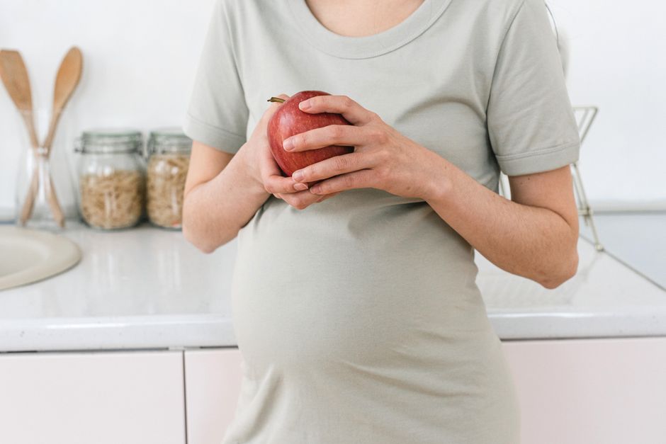 Gravid kvinna håller ett rött äpple i köket