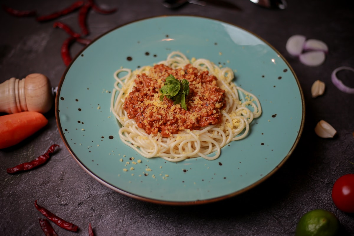 Spaghetti bolognese served on a teal plate with garnishes.